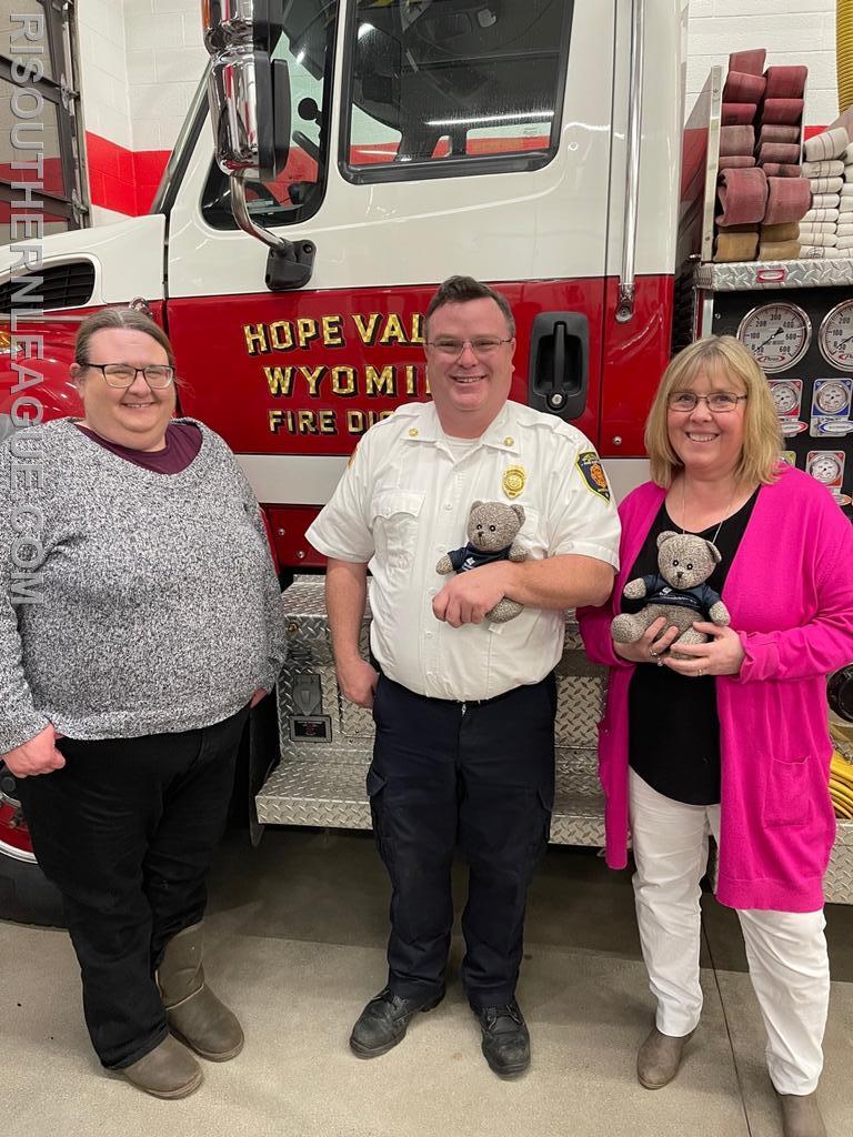 Chief Justin Lee, President of the Southern League poses with Margaret Teehan (left) and Lori Roeleveld (right) in front of Hope Valley Tanker 915 along with one of the teddy bears donated by TriCounty Community Action to the League's Departments. 